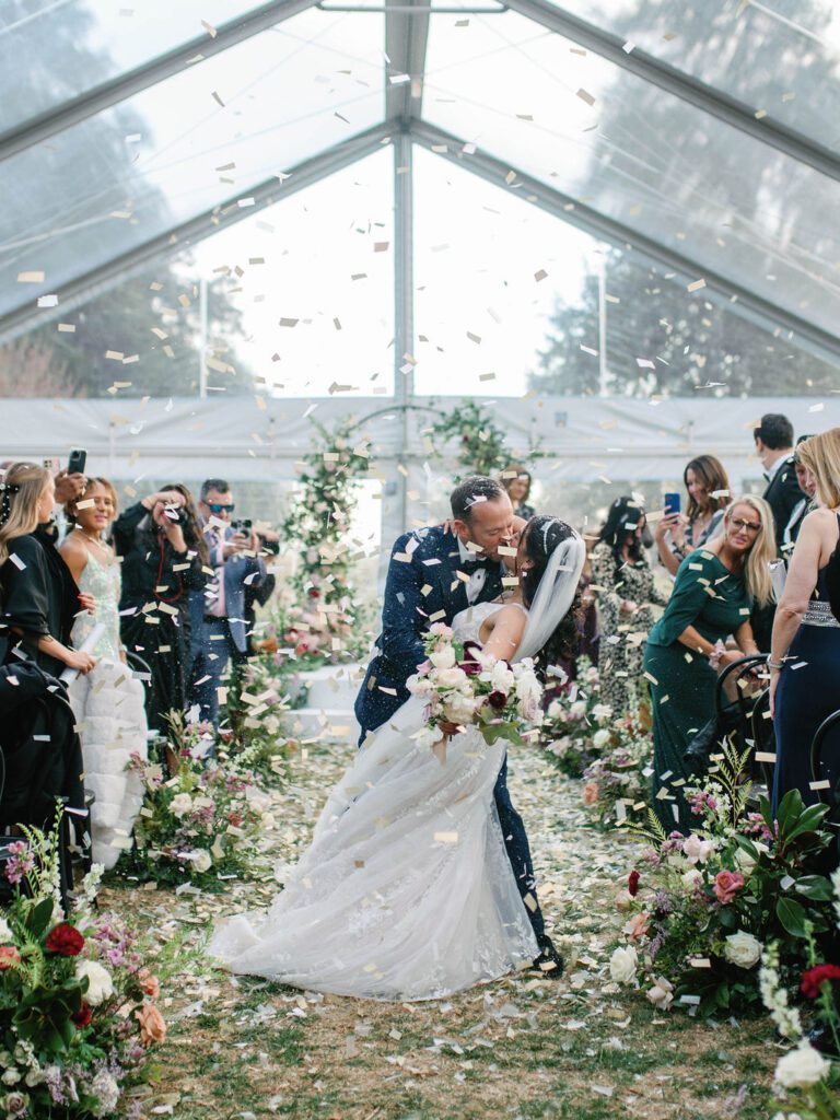 bride and groom kissing under white confetti at the end of their wedding ceremony at Whitehall Annapolis, planned by Maryland wedding planners, Nouvelle Weddings